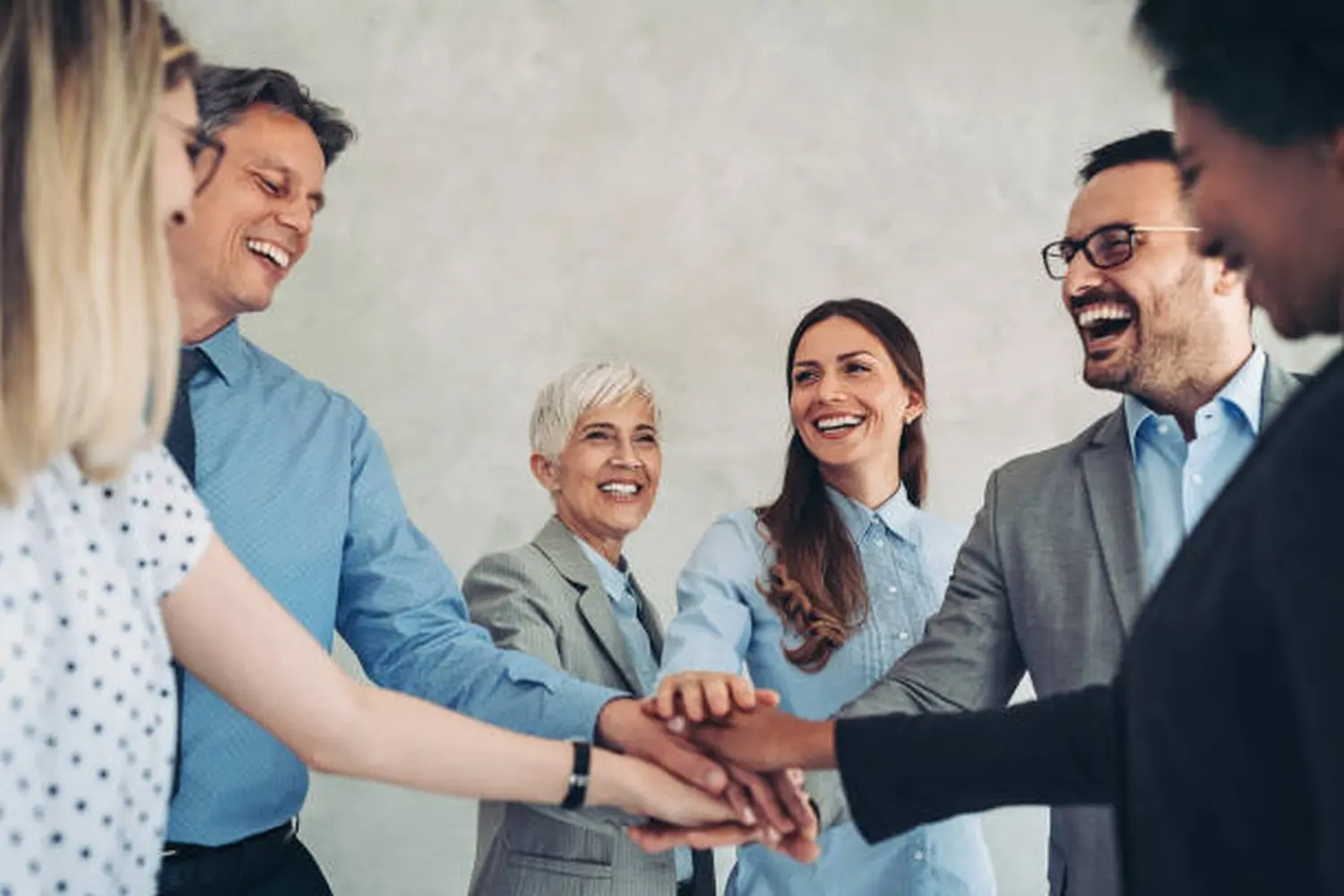 Porträt lachender Geschäftsleute mit gestapelten Händen für Missionsziele von Ziemlich bester Ruhestand