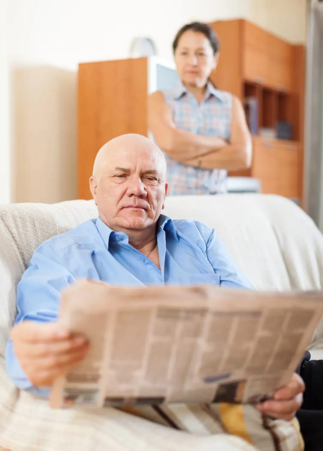 Reifer Mann liest Zeitung vor trauriger Frau. (Ziemlich bester Ruhestand)